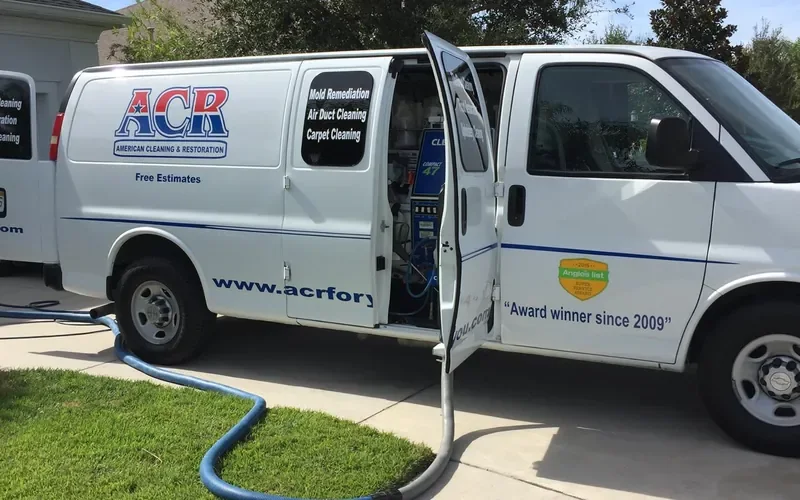 ACR van with its side door open and duct cleaning hose running across the lawn to the house