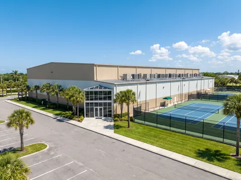 Indoor sports complex with rooftop AC units next to fenced tennis courts