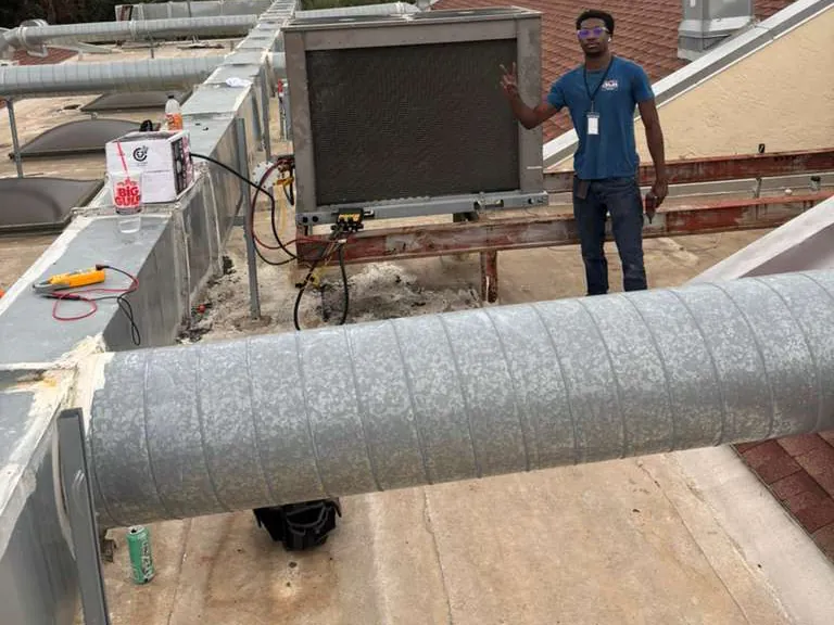 Technician on a flat roof behind a long round sheet metal duct