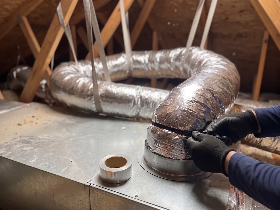 Gloved hands tightening a strap around flex duct on a plenum collar