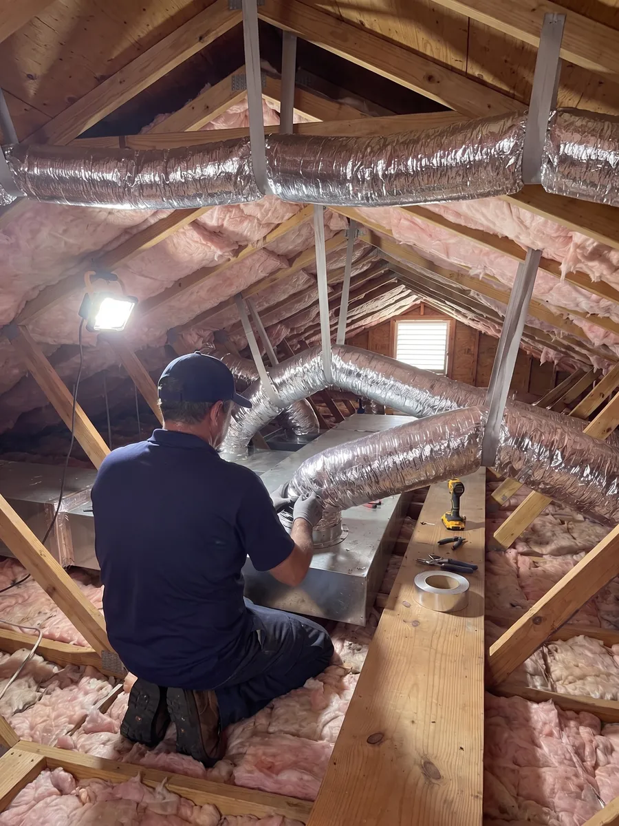 Technician connecting flex duct to a sheet metal plenum in an attic