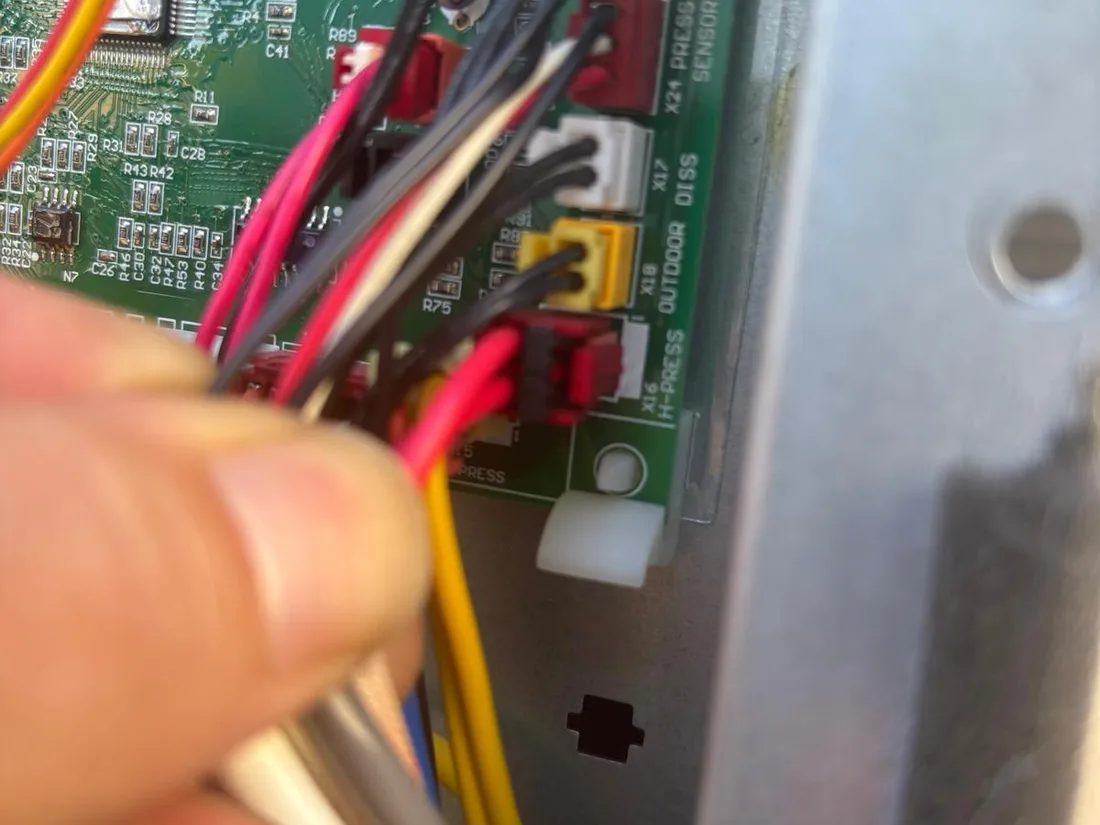 Technician checking wiring at an outdoor unit's control board during a diagnosis