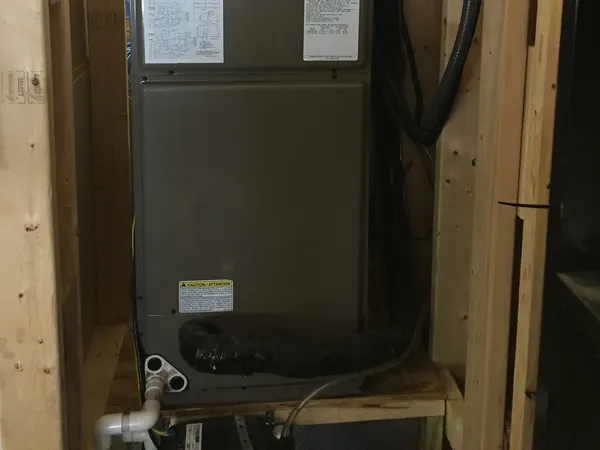 Air handler on a wooden stand with its PVC condensate drain line at the base