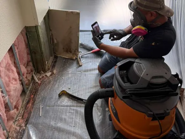 Technician in a respirator photographing stained wall framing after the lower drywall was cut out