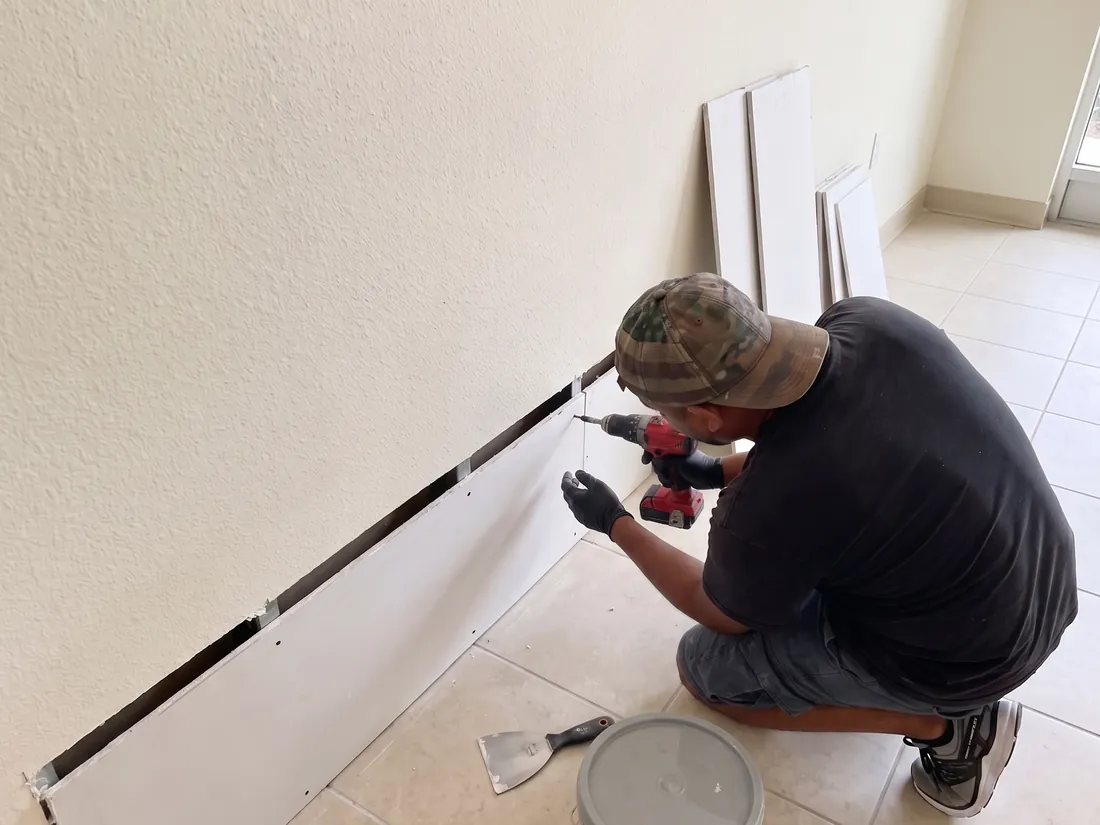 Technician fastening a new strip of drywall along the bottom of a wall